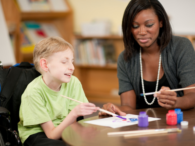 Generic image of a child with special needs painting with a teacher or teaching assistant