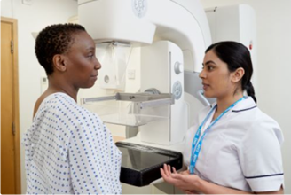 Photo of a lady in a hospital gown and a clinician by a mammogram machine